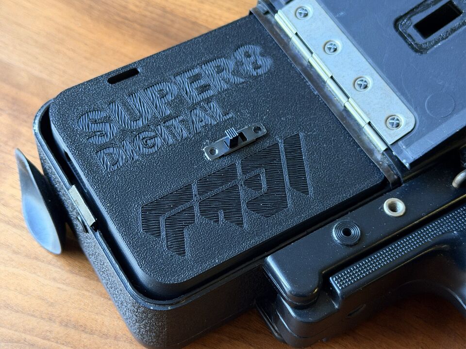 The cartridge seated in the film chamber of a Super 8 camera with the chamber door swung open.